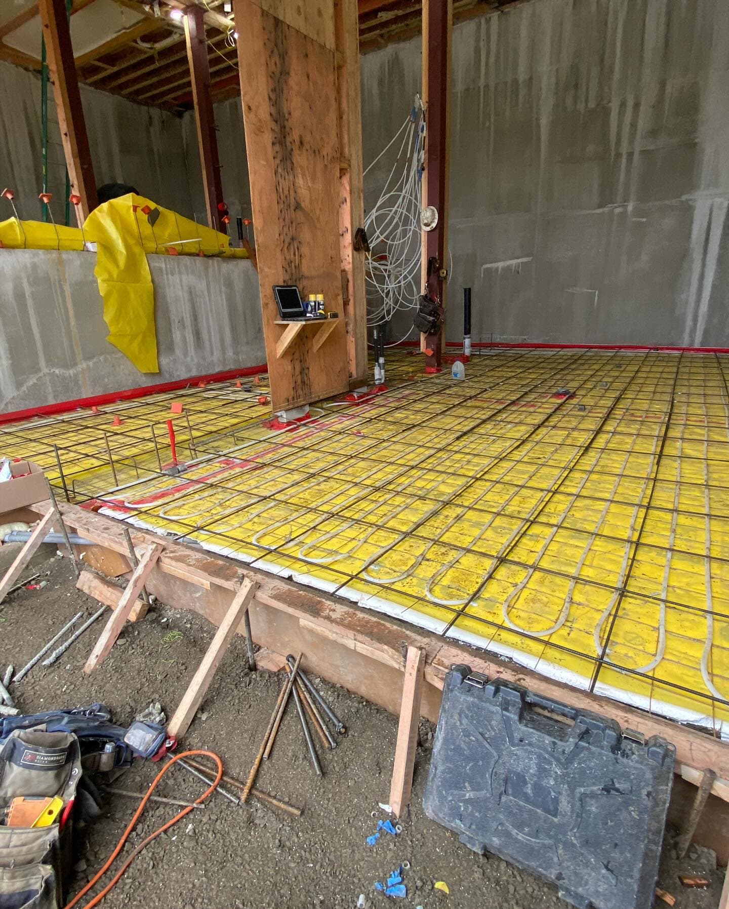 Radiant heat tubing laid in loops over yellow insulation board and rebar, ready for a slab pour inside a framed building.