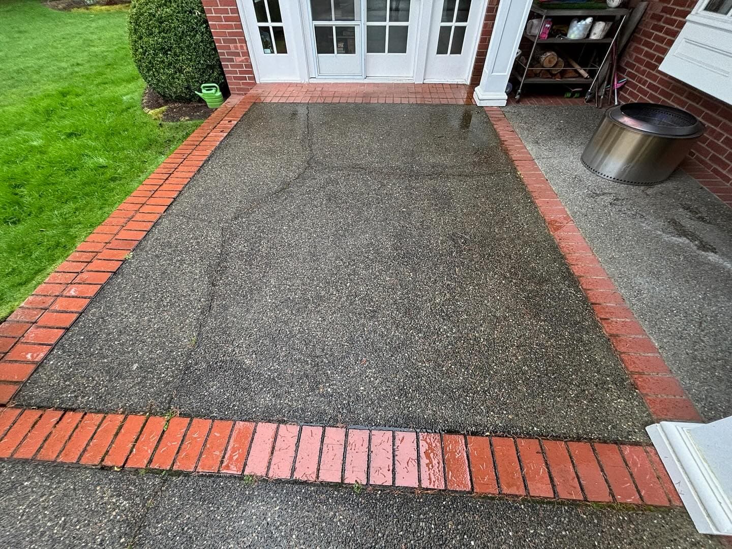 A finished patio with a fine, speckled sand finish framed by a red brick border, leading to white French doors.
